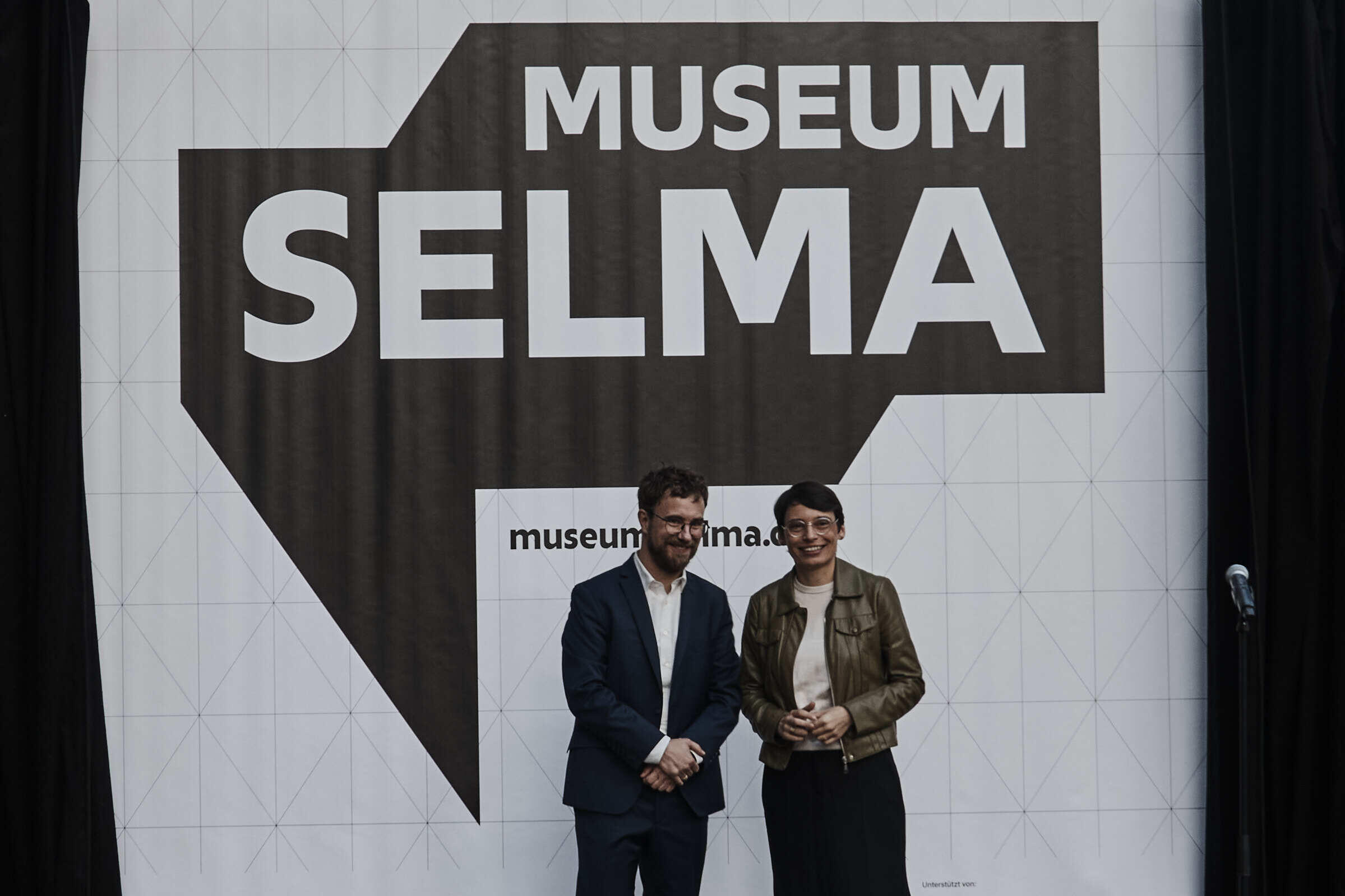 DOMiD-Geschäftsführer Dr. Robert Fuchs und NRW-Integrationsministerin Josefine Paul vor dem neuen Logo des Museums Selma.