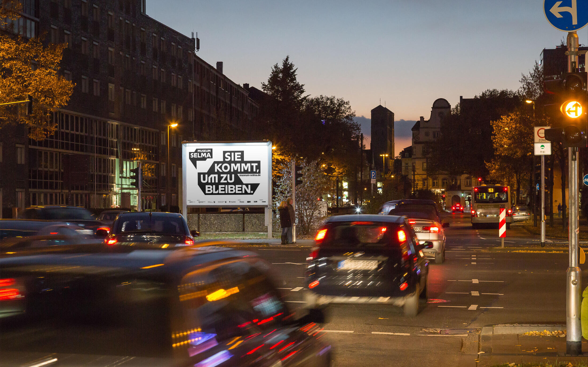 Ein beleuchtetes Werbeplakat für das Museum Selma, an einer Hauptstraße in Köln.